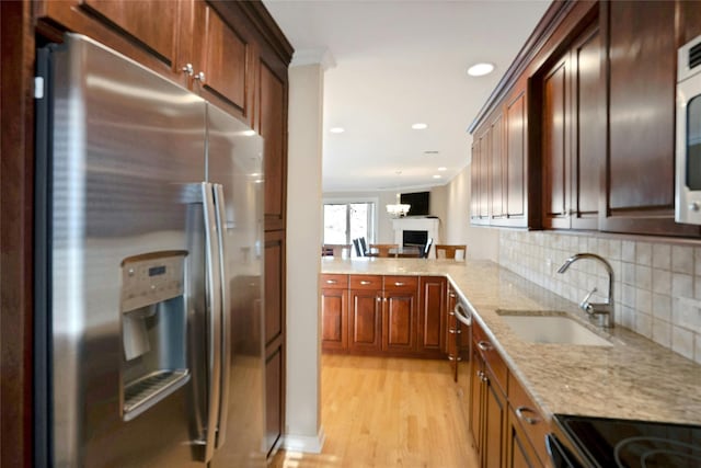 kitchen with light stone counters, a sink, decorative backsplash, light wood-style floors, and stainless steel fridge