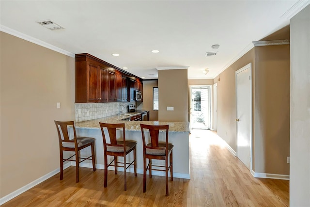 kitchen featuring visible vents, crown molding, decorative backsplash, light wood-style floors, and stainless steel appliances