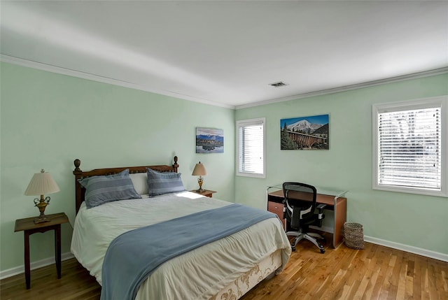 bedroom with visible vents, baseboards, wood finished floors, and ornamental molding