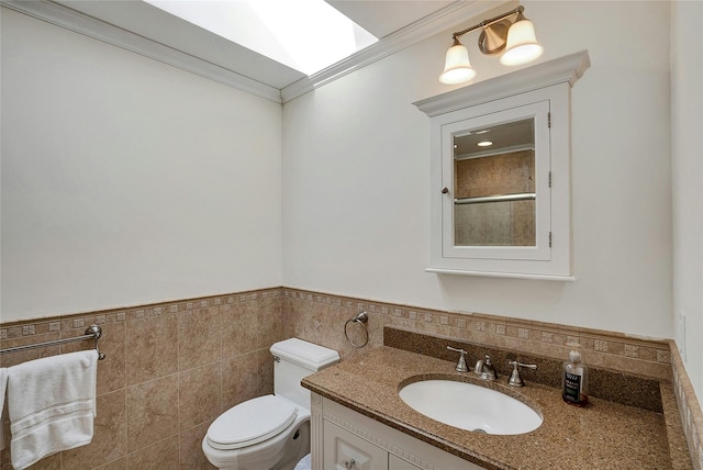 bathroom with vanity, a wainscoted wall, crown molding, toilet, and tile walls