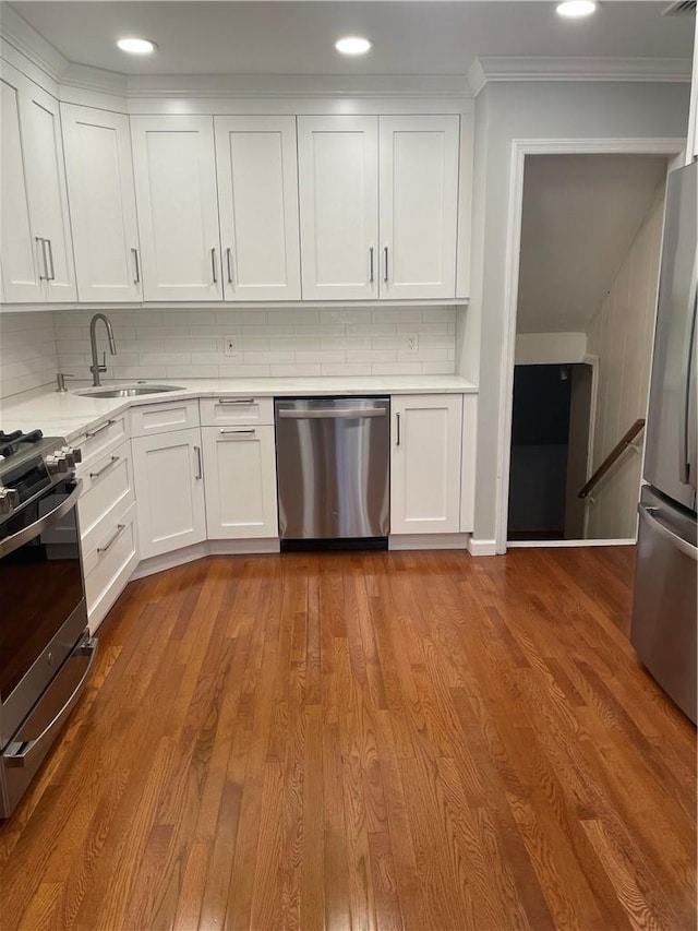 kitchen featuring light countertops, appliances with stainless steel finishes, white cabinets, a sink, and wood finished floors