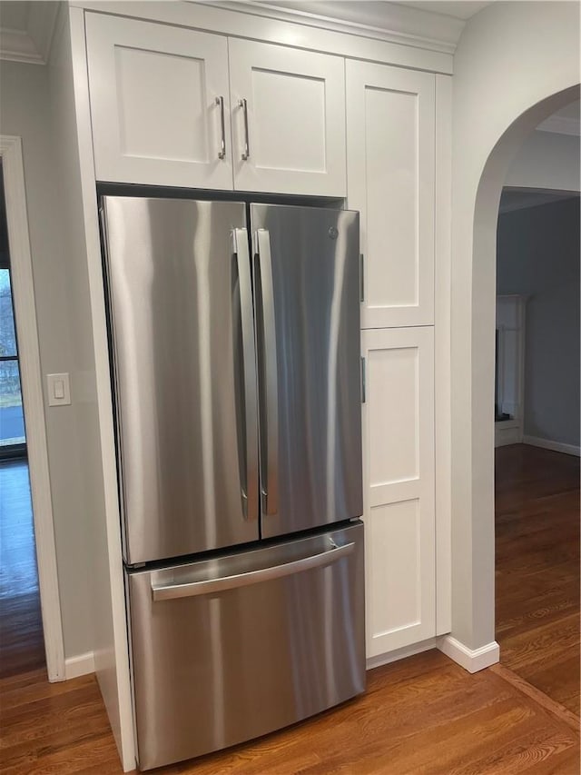 kitchen with arched walkways, wood finished floors, baseboards, white cabinets, and freestanding refrigerator