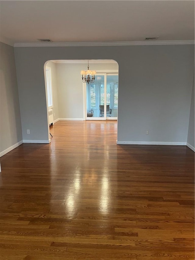 spare room featuring arched walkways, ornamental molding, dark wood-style flooring, and visible vents