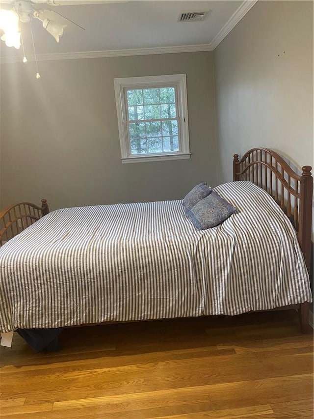 bedroom with a ceiling fan, visible vents, wood finished floors, and ornamental molding