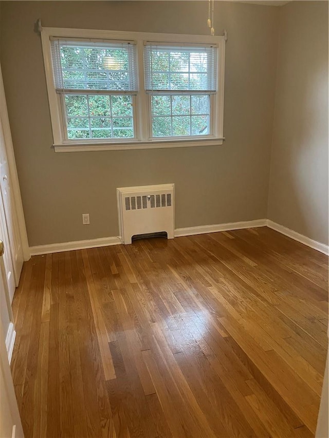 empty room with radiator heating unit, hardwood / wood-style flooring, and baseboards