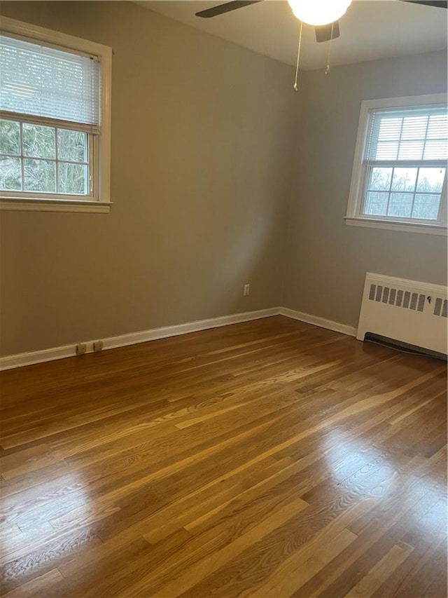 unfurnished room with baseboards, dark wood-style flooring, a ceiling fan, and radiator