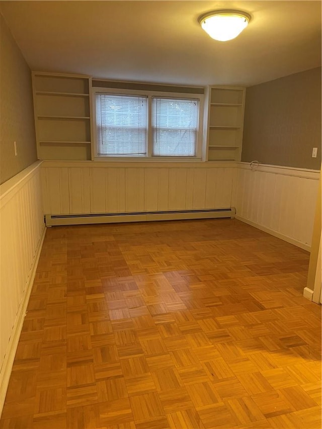 unfurnished room with built in shelves, baseboard heating, and wainscoting