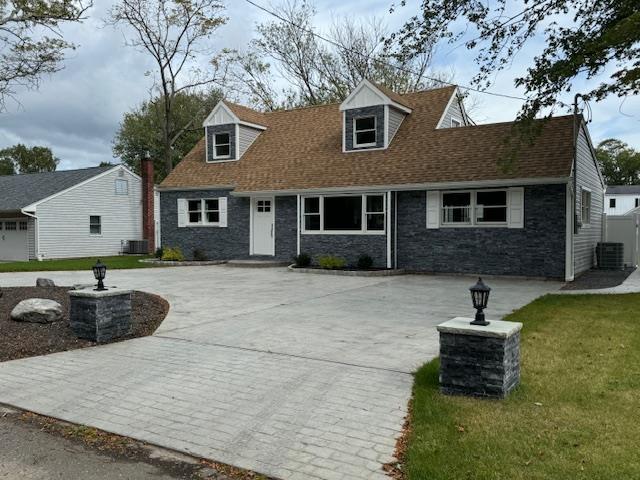 cape cod house featuring stone siding, a front lawn, curved driveway, and a shingled roof