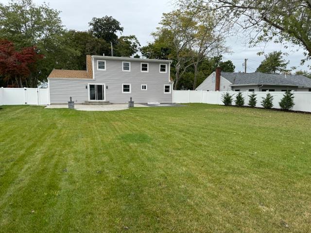 rear view of house with a patio area, a fenced backyard, a yard, and a chimney