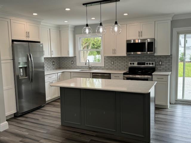 kitchen with dark wood-style flooring, a center island, stainless steel appliances, light countertops, and a sink