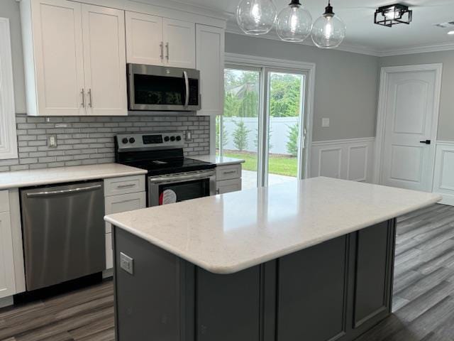 kitchen featuring stainless steel appliances, wood finished floors, white cabinetry, wainscoting, and crown molding