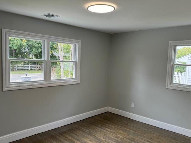 empty room with dark wood-style floors, visible vents, and baseboards