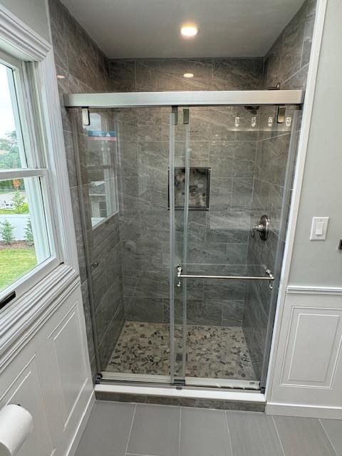 full bath with wainscoting, a shower stall, and a decorative wall