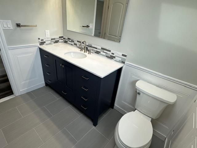 bathroom featuring tile patterned flooring, a wainscoted wall, vanity, and toilet