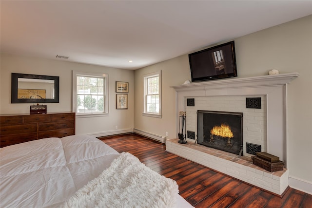 bedroom featuring a baseboard heating unit, a brick fireplace, dark wood-type flooring, baseboards, and recessed lighting