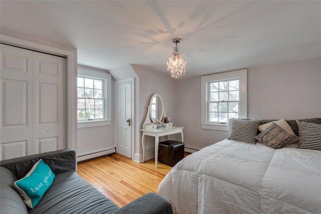 bedroom with baseboard heating, wood finished floors, a chandelier, and lofted ceiling