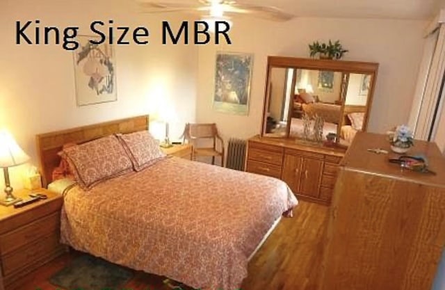 bedroom featuring ceiling fan, radiator heating unit, and wood finished floors