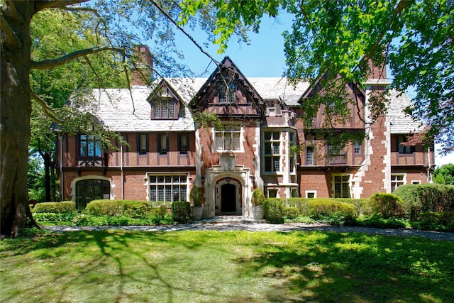 tudor-style house with a front yard, brick siding, and a chimney