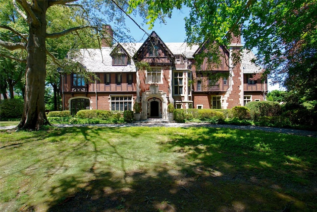 tudor home featuring a chimney, a front lawn, and brick siding