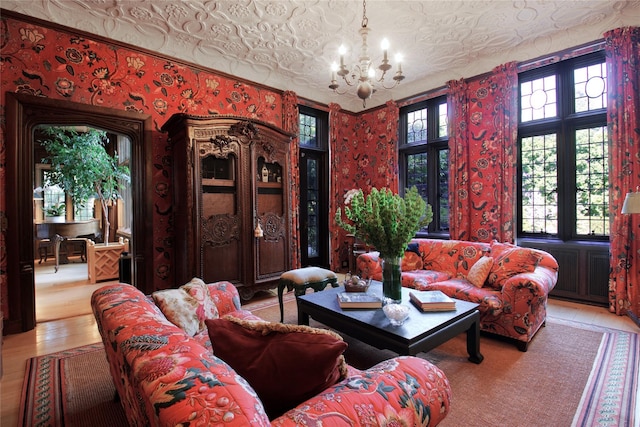 living room featuring wallpapered walls, an ornate ceiling, wood finished floors, and an inviting chandelier