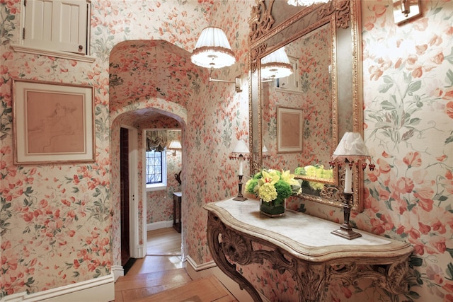 hall with arched walkways, light wood-style flooring, baseboards, and wallpapered walls