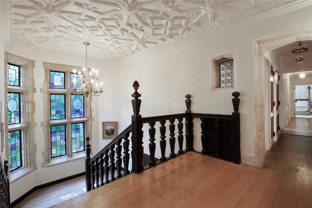 hallway with a chandelier, an upstairs landing, baseboards, ornamental molding, and an ornate ceiling