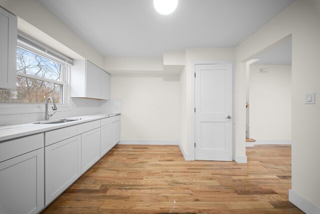 kitchen featuring baseboards, light countertops, a sink, and light wood-style floors