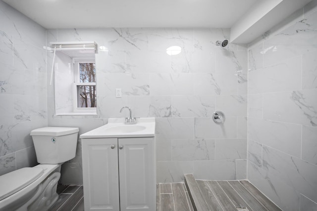 bathroom with tile walls, tiled shower, vanity, and toilet