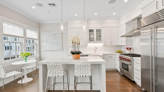 kitchen with dark wood-style flooring, light countertops, a sink, high quality appliances, and wall chimney exhaust hood