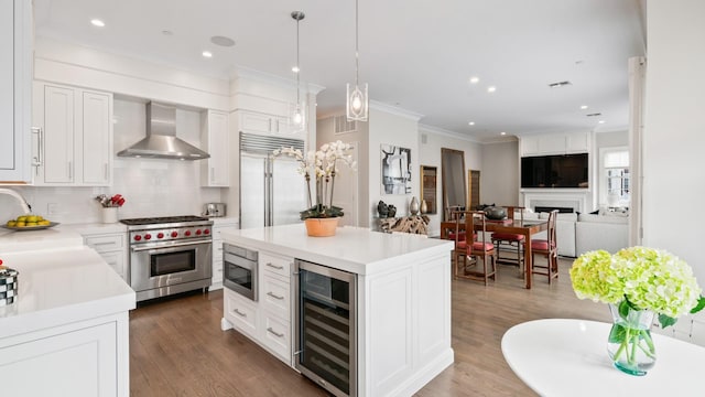 kitchen with beverage cooler, wood finished floors, built in appliances, wall chimney range hood, and a fireplace