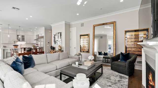 living area with light wood finished floors, recessed lighting, visible vents, ornamental molding, and a warm lit fireplace