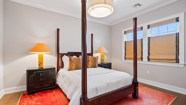 bedroom featuring visible vents, baseboards, wood finished floors, and ornamental molding