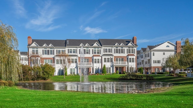 rear view of house featuring a water view and a lawn