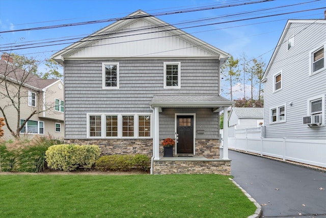 view of front of home featuring a front yard, stone siding, cooling unit, and fence