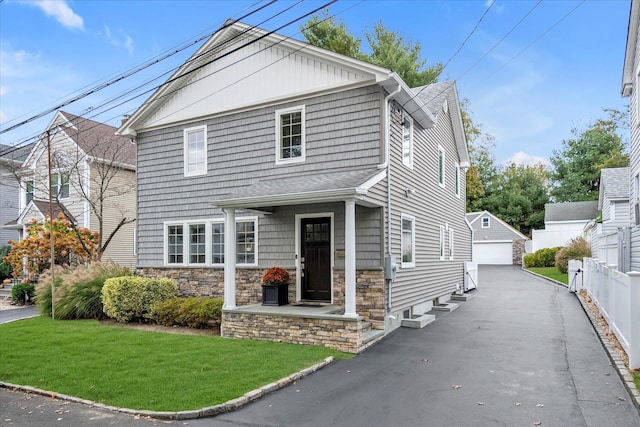 view of front of home with an outdoor structure, fence, a detached garage, stone siding, and a front yard