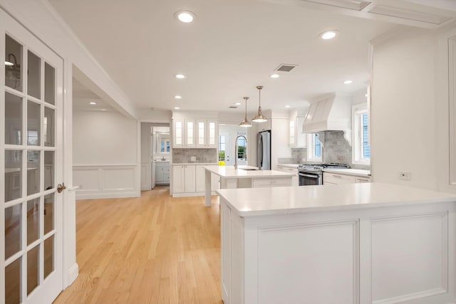 kitchen with visible vents, decorative backsplash, light wood-style flooring, appliances with stainless steel finishes, and custom exhaust hood