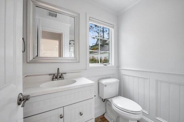 bathroom featuring toilet, vanity, visible vents, ornamental molding, and wainscoting