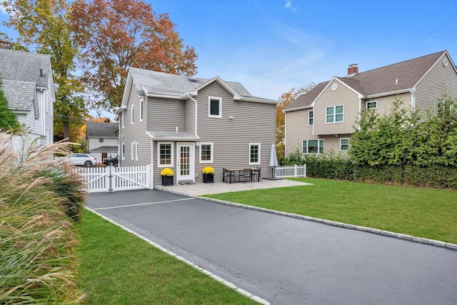 back of property featuring a lawn, aphalt driveway, a gate, fence, and a patio area