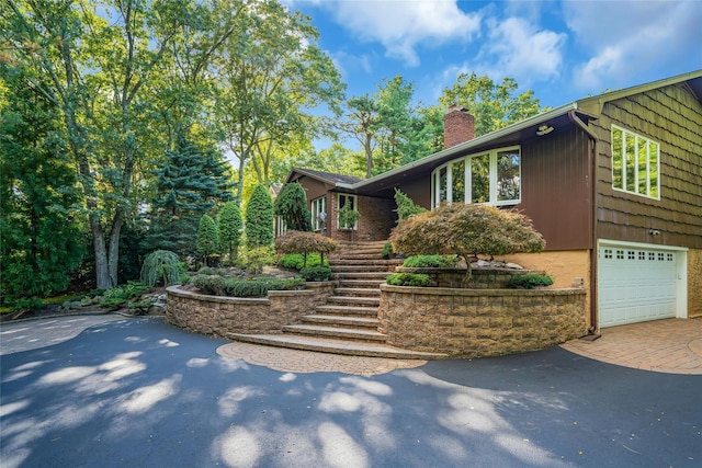 view of home's exterior with stairs, decorative driveway, a chimney, and a garage