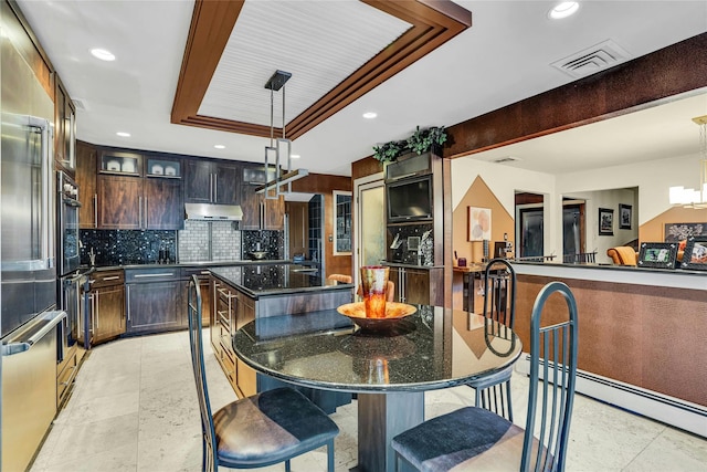 kitchen with a kitchen island, visible vents, backsplash, a tray ceiling, and dark stone countertops