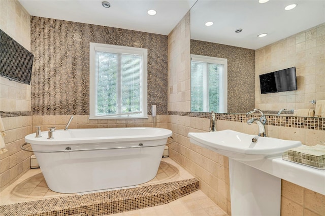 bathroom featuring a wealth of natural light, a soaking tub, and tile walls