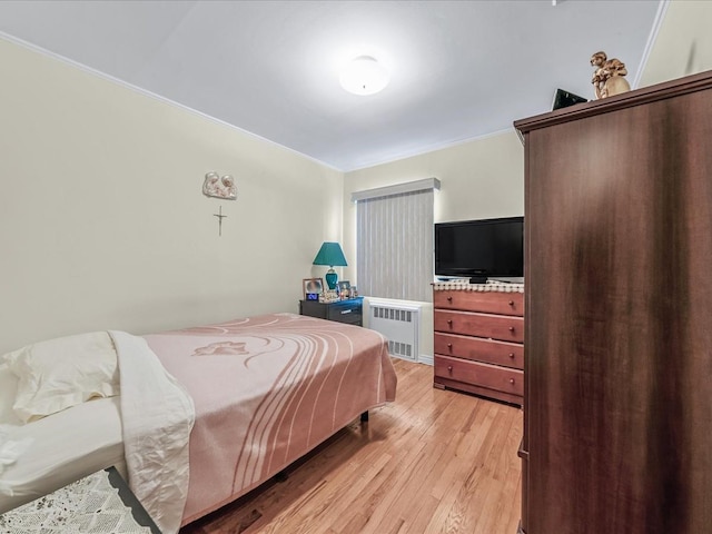 bedroom featuring crown molding, radiator heating unit, and light wood-type flooring