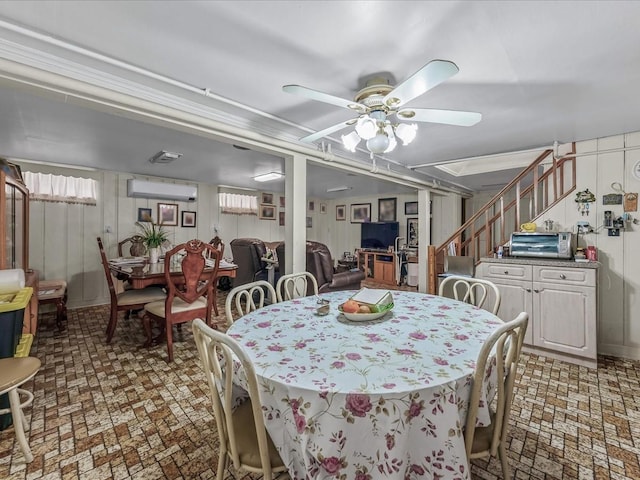 dining space featuring stairway, brick patterned floor, a ceiling fan, and a wall unit AC