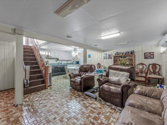 living area featuring brick floor, a ceiling fan, and stairs