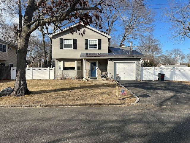 traditional home with an attached garage, roof mounted solar panels, fence, and aphalt driveway