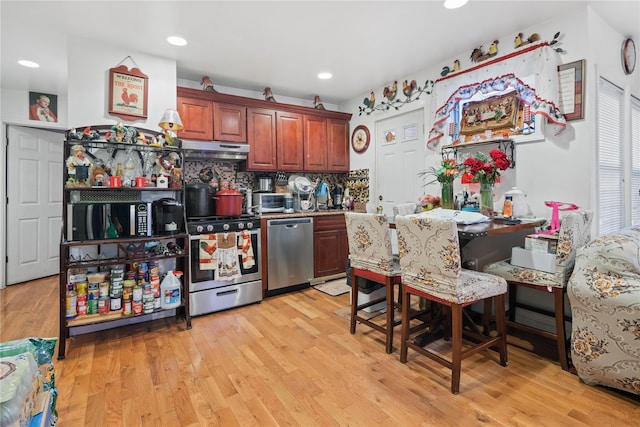 kitchen with under cabinet range hood, stainless steel appliances, tasteful backsplash, and light wood-style floors