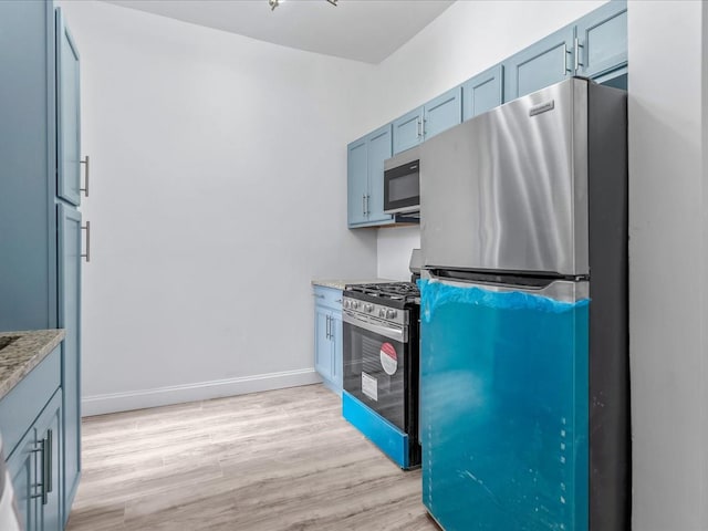 kitchen featuring light wood finished floors, appliances with stainless steel finishes, light stone countertops, blue cabinets, and baseboards