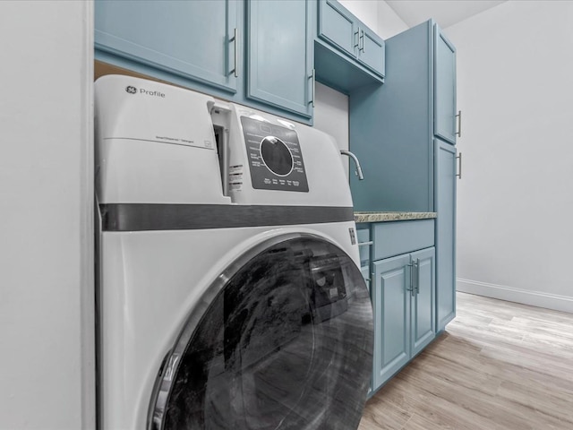 laundry room featuring baseboards, washer / clothes dryer, cabinet space, and light wood-style floors