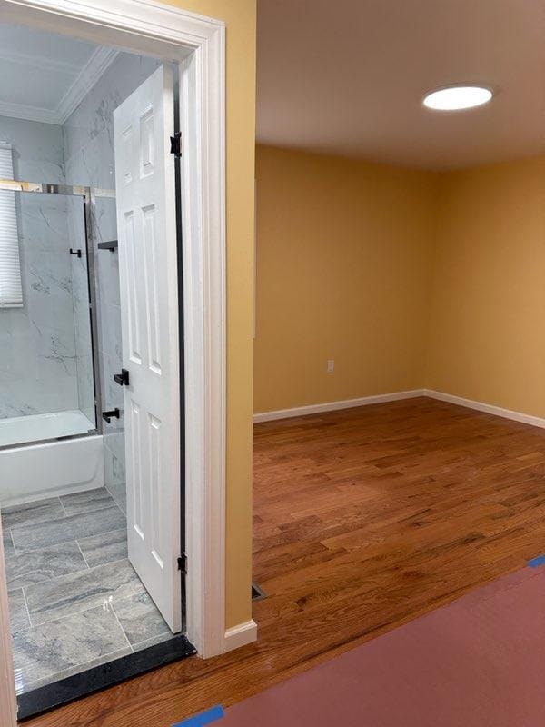 bathroom featuring ornamental molding, enclosed tub / shower combo, baseboards, and wood finished floors