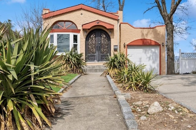 view of exterior entry with stucco siding, french doors, concrete driveway, and a garage